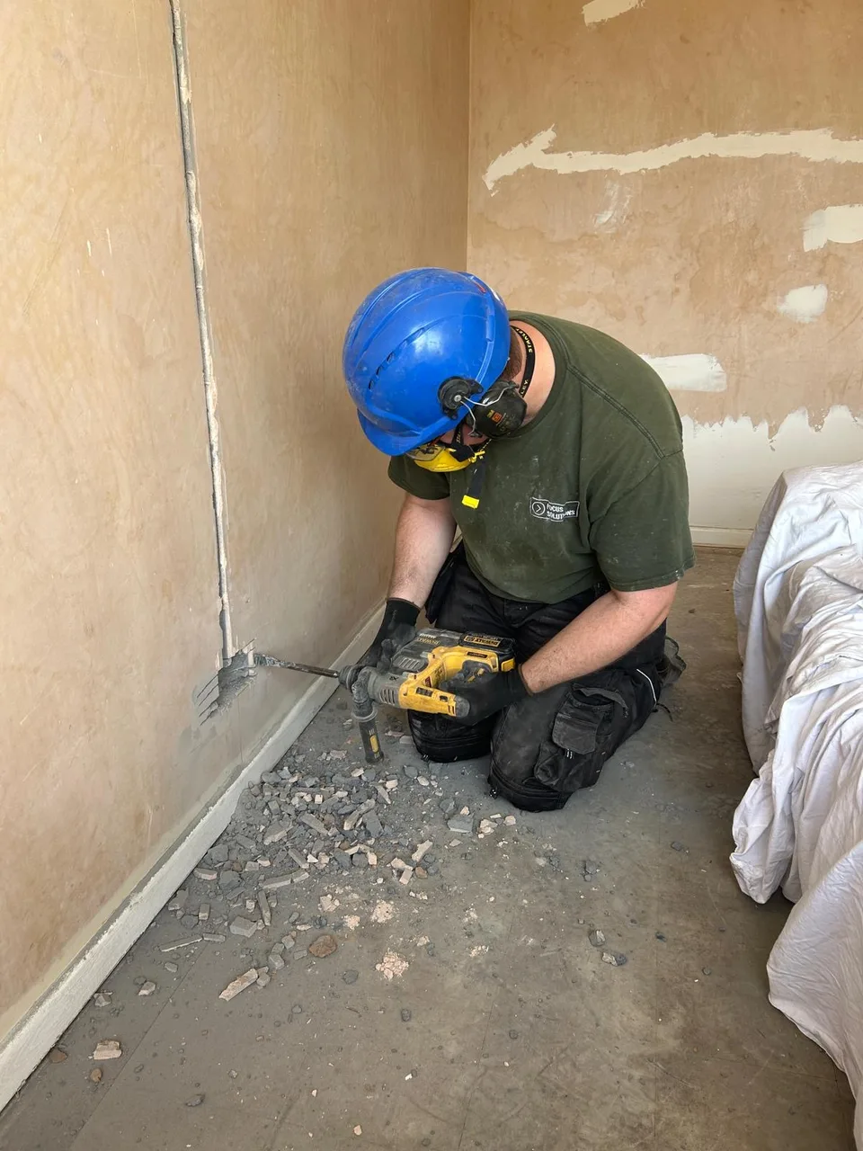Bradley in work PPE kneeling to chase a cable channel into a plastered wall