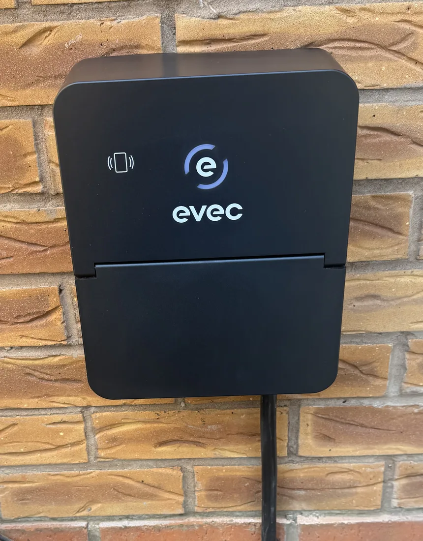 Black EVEC charge point installed on a brick wall with cabling routed down beneath it
